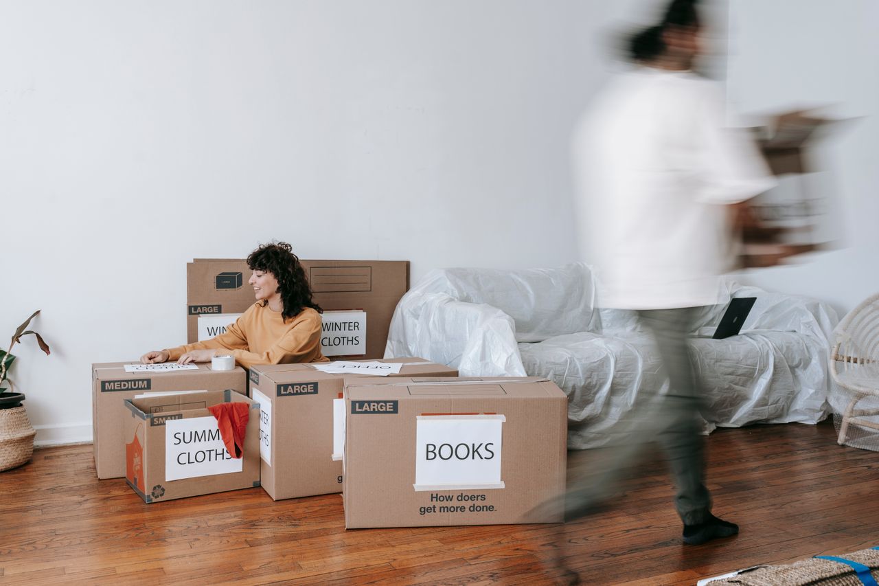 our-mission A couple packing labeled boxes in a minimalist living room, preparing for moving day.